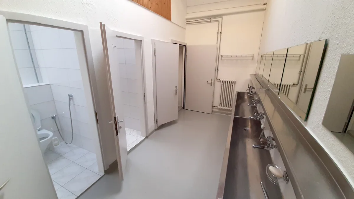 Blick in eine WC-Anlage mit einem langen Lavabo aus Chromstahl. 
